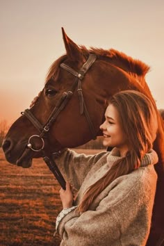 a woman standing next to a brown horse on top of a dry grass covered field