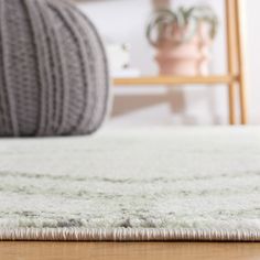 a white rug on top of a wooden floor next to a chair and potted plant