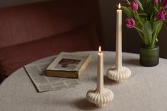 two candles sitting on top of a table next to a vase filled with pink flowers