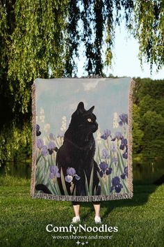 a black cat sitting on top of a lush green field next to a tree with purple flowers