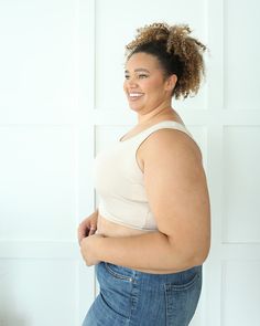 a woman with her arms around her waist, smiling at the camera while standing in front of a white wall