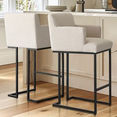 two white chairs sitting on top of a wooden floor in front of a kitchen counter