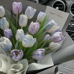 a bouquet of white and purple tulips sitting on top of a car dashboard