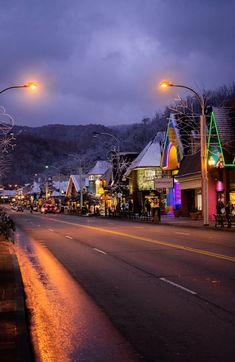 an empty street at night with lights on and buildings lit up in the background,