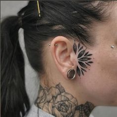 a woman with black tattoos on her neck and behind the ear is a rose tattoo