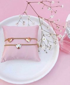 two bracelets sitting on top of a white plate next to a pink flower vase