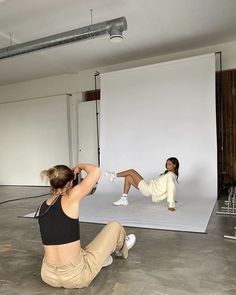 two women sitting on the floor in front of a white backdrop with one woman doing yoga