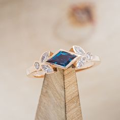 a gold ring with a blue stone surrounded by white and clear stones on a wooden stand