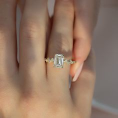 a woman's hand with a diamond ring on top of her finger and an emerald stone in the middle