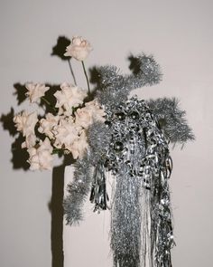 a vase filled with white flowers next to a silver tinsel covered planter on a table