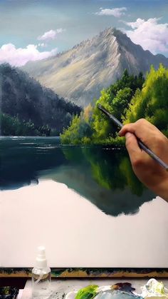 a person is holding a paintbrush in their hand and painting a landscape with mountains