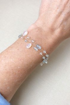 This bracelet showcases delicate moss aquamarine gemstones paired with radiant rainbow moonstones, creating a lovely, feminine style. The artisan meticulously hand-wire-wraps each gemstone bead, creating a beautiful, double-layered chain. The lobster claw clasp and extender chain allow for an adjustable fit. Bracelet length: 7 inches plus 1-inch extender chain Materials: aquamarine, rainbow moonstone, gold fll Hand Wrapped Moonstone Bracelet, Elegant Hand-strung Aquamarine Jewelry, Dainty Moonstone Jewelry With Gemstone Beads, Elegant Hand-strung Moonstone Jewelry, Elegant Hand Wrapped Moonstone Jewelry, Elegant Hand-wrapped Moonstone Jewelry, Moss Aquamarine, Layered Chain, The Lobster