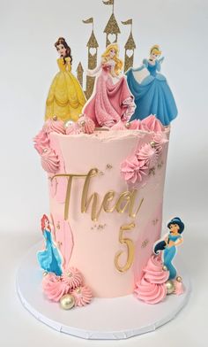 there is a pink cake with princesses on it and the number five in gold