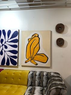 three paintings hang on the wall next to a yellow couch and two other art pieces