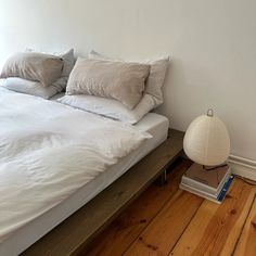 a bed with white sheets and pillows on top of it next to a wooden floor