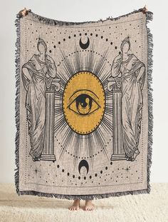 a tapestry with an all seeing eye in the center and two women standing behind it