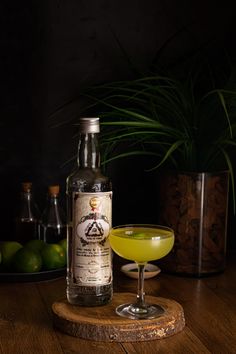 a bottle of alcohol sitting next to a glass filled with liquid and limes on a wooden table