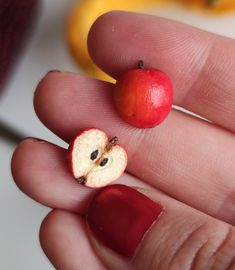 a person's hand holding a tiny apple with a bite taken out of it