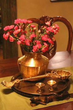 pink flowers are in a gold vase on a tray next to candles and spoons