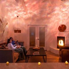 two people sitting on a couch in front of a fire place with candles around them