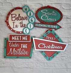 four christmas signs hanging on the wall in front of a white brick wall with red and green lettering