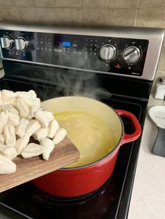 a pot full of food sitting on top of a stove next to a wooden cutting board