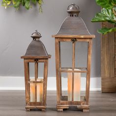 two wooden lanterns sitting next to each other on top of a floor near a potted plant