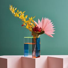 a vase filled with colorful flowers on top of a white table next to a green wall