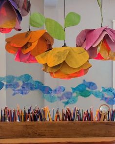 colorful paper flowers hanging from the ceiling in front of a table with pencils on it