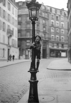 a black and white photo of a person standing on a street light in an old city