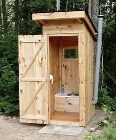 a wooden outhouse in the woods with its door open to reveal a small toilet