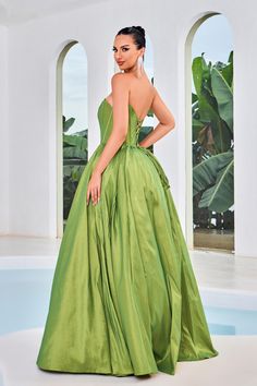 a woman in a long green dress standing by a pool with her back to the camera