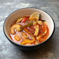 a bowl filled with soup and vegetables on top of a stone counter next to a slice of lemon