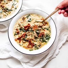 two bowls of soup with spinach and meat in them on a white tablecloth