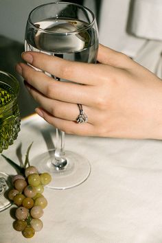 a woman's hand holding a wine glass with grapes on the table next to it