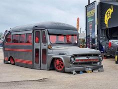 an old school bus is parked in a lot next to other cars and trucks at a car show