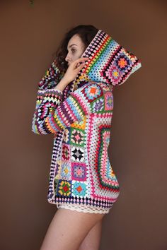 a woman in a colorful crocheted jacket is holding her hood up to her face