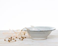 a white bowl sitting on top of a wooden table next to a chain and flowers