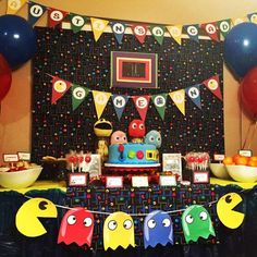 a birthday cake with pacman decorations and balloons on the wall in front of it