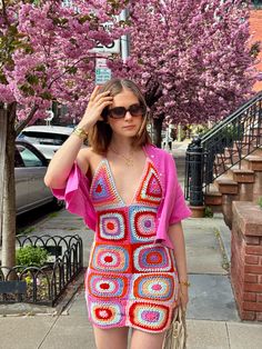 a woman in a crocheted dress is standing on the sidewalk with her hand up to her head