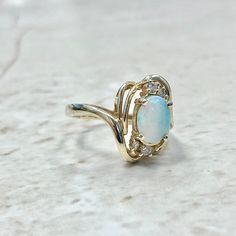 CLEARANCE - 40% OFF! Lovely vintage 14 karat yellow gold ring featuring an oval opal cabochon weighing approximately 1/2 carat, and 4 single cut diamonds weighing approximately 0.06 carat. The diamonds are near colorless and are slightly included to Included. Ring size 6.25 US / M UK / 52 FR. > Resizing not included. This ring can be resized to fit most fingers. Please contact us for details. Resized rings are final sale. Weighs 4.4 grams. Condition: Very Good. Minor scratches throughout metal. Fine Jewelry Oval Cabochon Opal Ring, Oval Cabochon Opal Ring Fine Jewelry, Oval Cabochon Opal Ring In Fine Jewelry, Heirloom Oval Cabochon Opal Ring, Heirloom Oval Opal Ring For Formal Occasions, Oval Opal Ring For Anniversary, 14k Yellow Gold Opal Ring With Diamond Accents, Heirloom Oval Moonstone Ring With Multi-stone, Gold Oval Opal Birthstone Ring