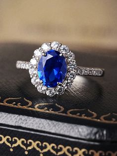 a blue and white diamond ring sitting on top of a black leather box next to a book