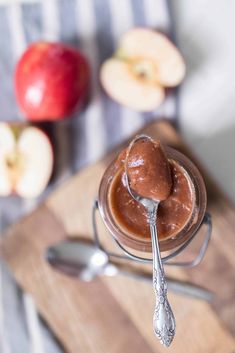 a spoon full of peanut butter on top of an apple and another apples in the background