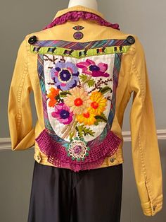 a woman's yellow jacket with colorful flowers on the front and back, sitting on a mannequin