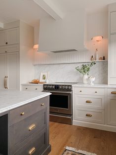 a kitchen with white cabinets and marble counter tops, gold pulls on the oven hood