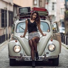 a woman sitting on top of an old vw bug in the middle of a cobblestone street