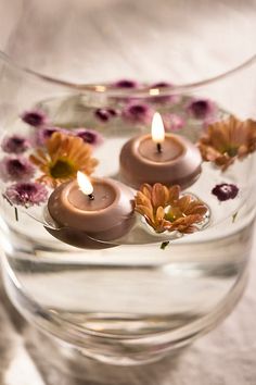 three lit candles floating in water with flowers