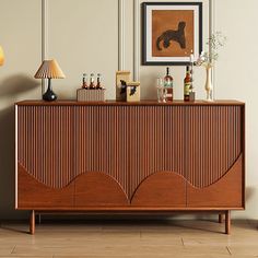 a wooden cabinet with bottles on it in a room next to a lamp and pictures