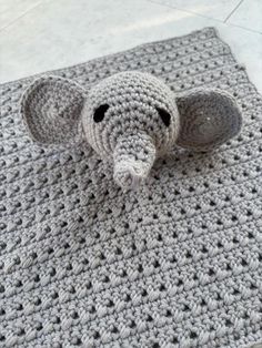 a crocheted elephant sitting on top of a gray rug next to a white tile floor