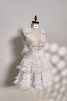 a white dress with ruffles and beads on the neckline is sitting on a mannequin